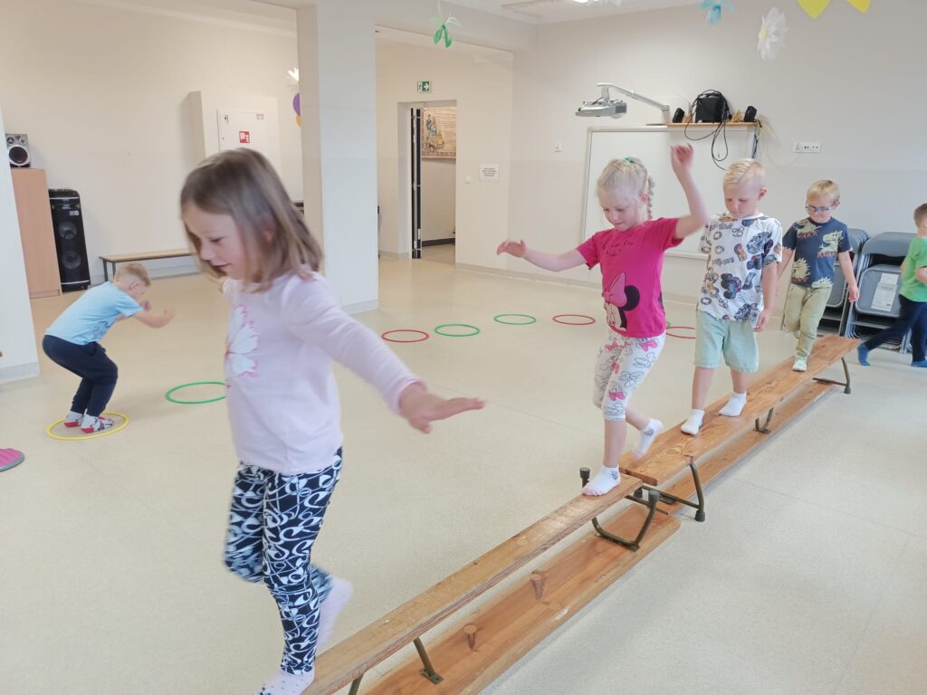 Dzieci ćwiczą na sali gimnastycznej pokonują tor przeszkód