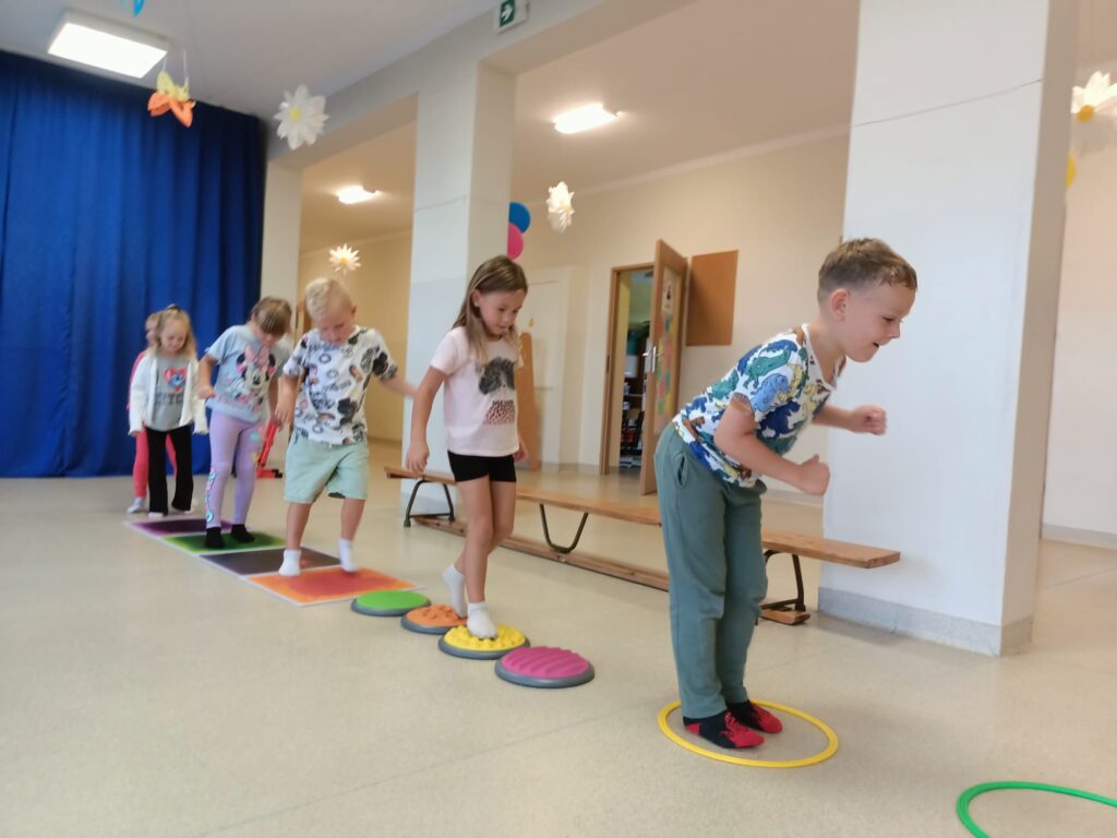Dzieci ćwiczą na sali gimnastycznej pokonują tor przeszkód