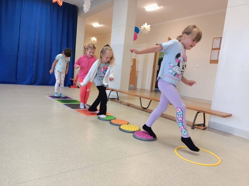 Dzieci ćwiczą na sali gimnastycznej pokonują tor przeszkód