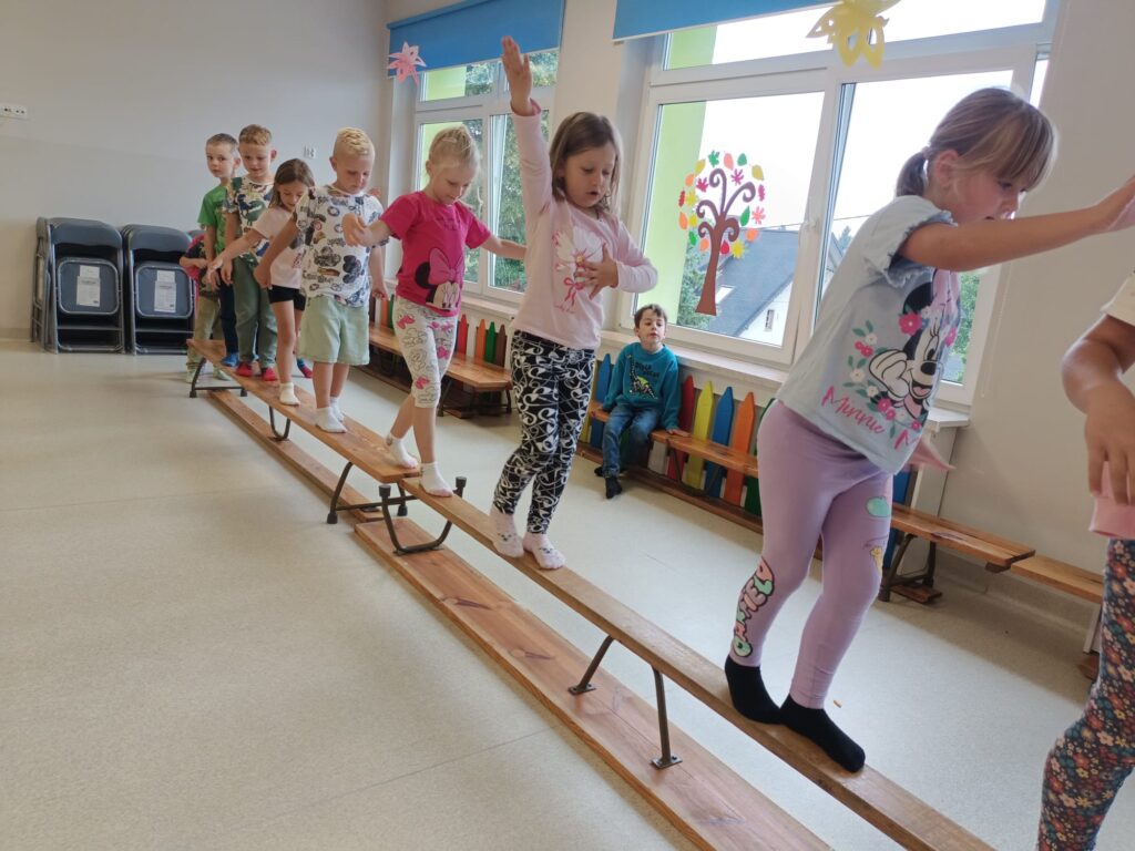 Dzieci ćwiczą na sali gimnastycznej pokonują tor przeszkód