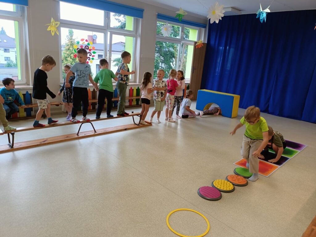 Dzieci ćwiczą na sali gimnastycznej pokonują tor przeszkód