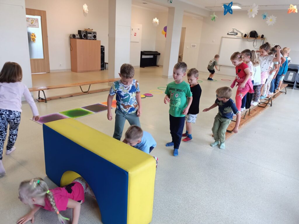 Dzieci ćwiczą na sali gimnastycznej pokonują tor przeszkód