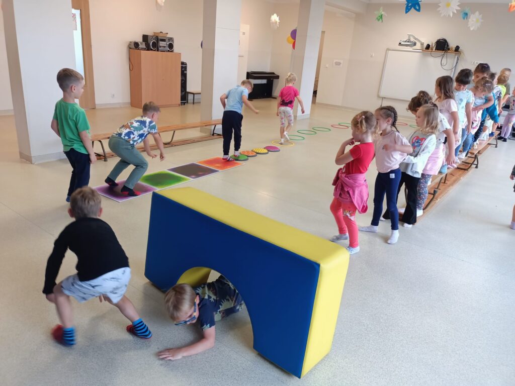 Dzieci ćwiczą na sali gimnastycznej pokonują tor przeszkód