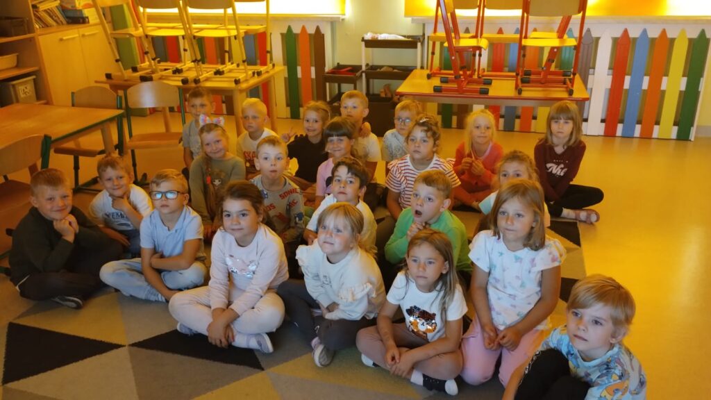 Przedszkolaki siedzą na dywanie słuchają prelekcji