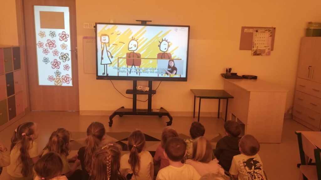 Przedszkolaki siedzą na dywanie słuchają prelekcji