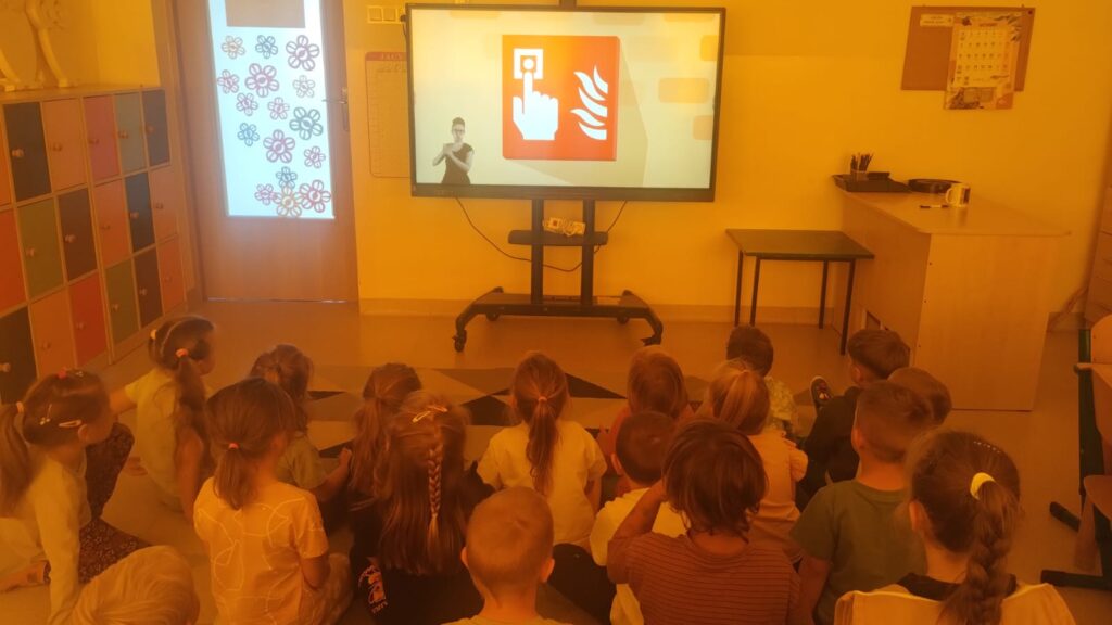 Przedszkolaki siedzą na dywanie słuchają prelekcji