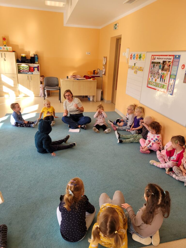 Przedszkolaki siedzą na dywanie słuchają prelekcji
