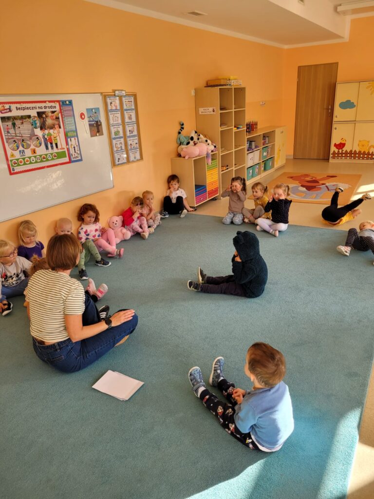 Przedszkolaki siedzą na dywanie słuchają prelekcji