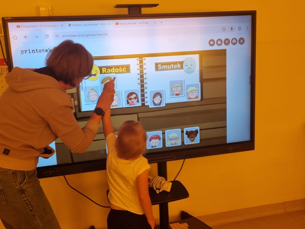 Dziecko i nauczyciel korzysta z tablicy multimedialnej