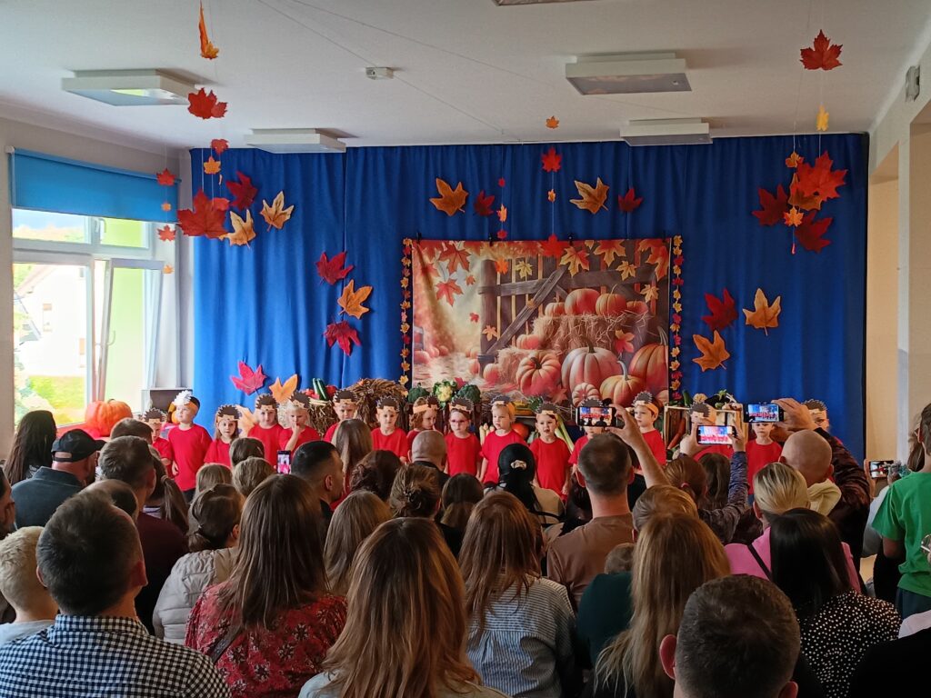 Grupa 3 latków występuje przed publicznością, dzieci śpiewają i tańczą