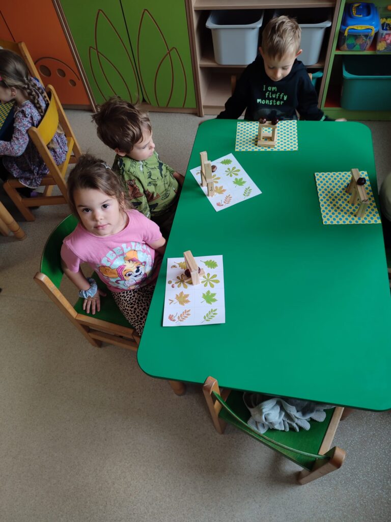 Dzieci konstruują rożne drzewa przy użyciu klocków drewnianych i kasztanów.