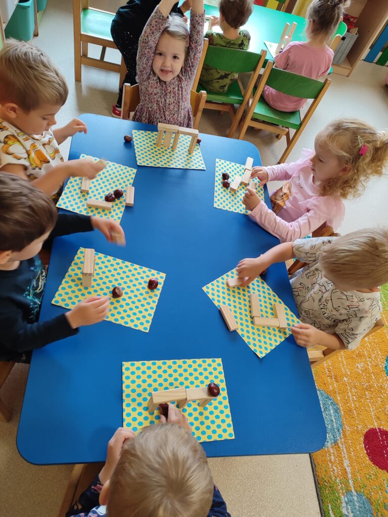 Dzieci konstruują rożne drzewa przy użyciu klocków drewnianych i kasztanów.