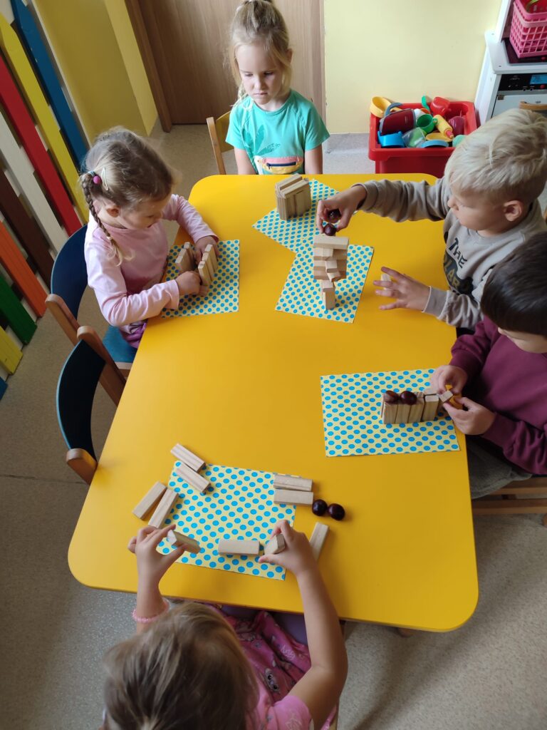 Dzieci konstruują rożne drzewa przy użyciu klocków drewnianych i kasztanów.