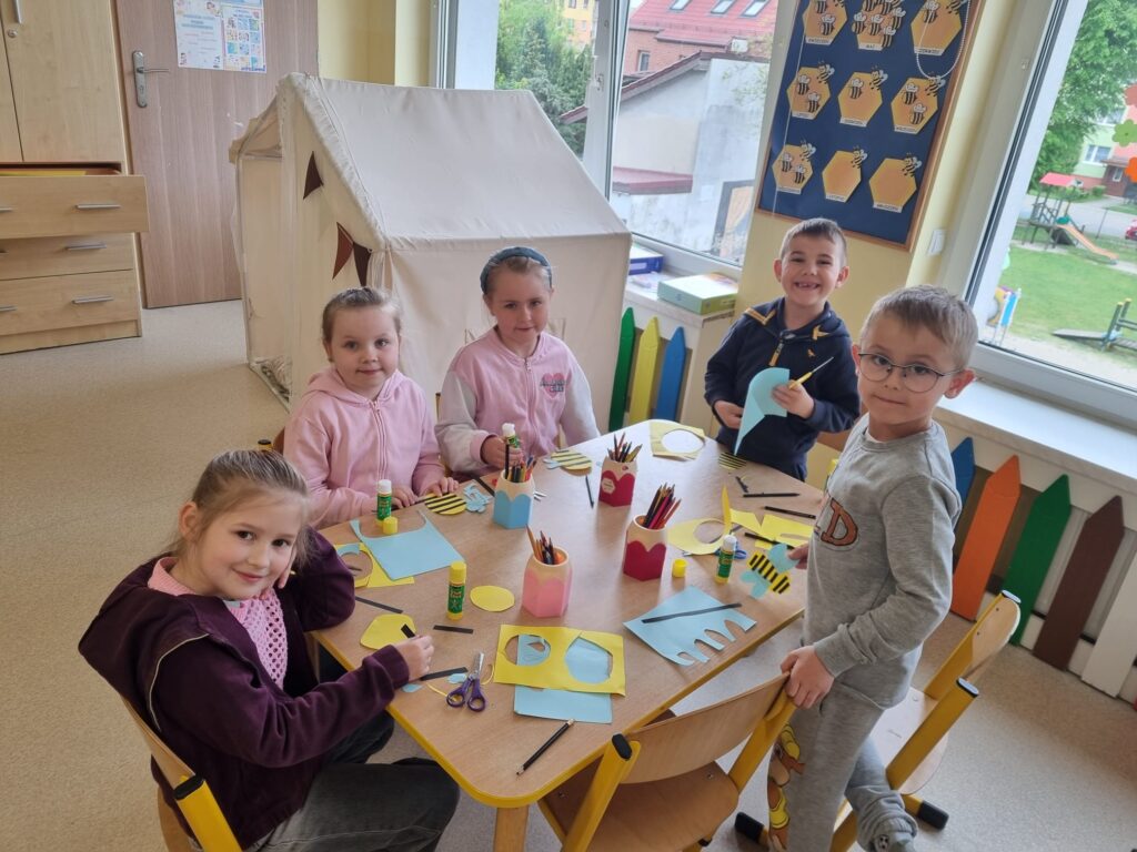 Dzieci siedzą przy stolikach i wykonują prace plastczyną.