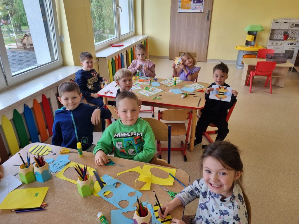 Dzieci siedzą przy stolikach i wykonują prace plastcyzną.
